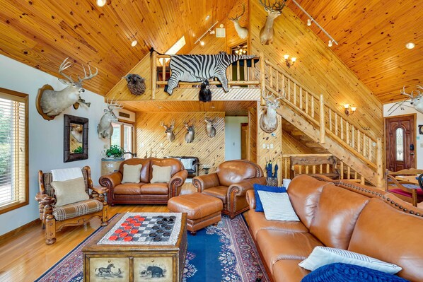 A spacious living room with leather furniture, a wooden ceiling, and various mounted animal heads.