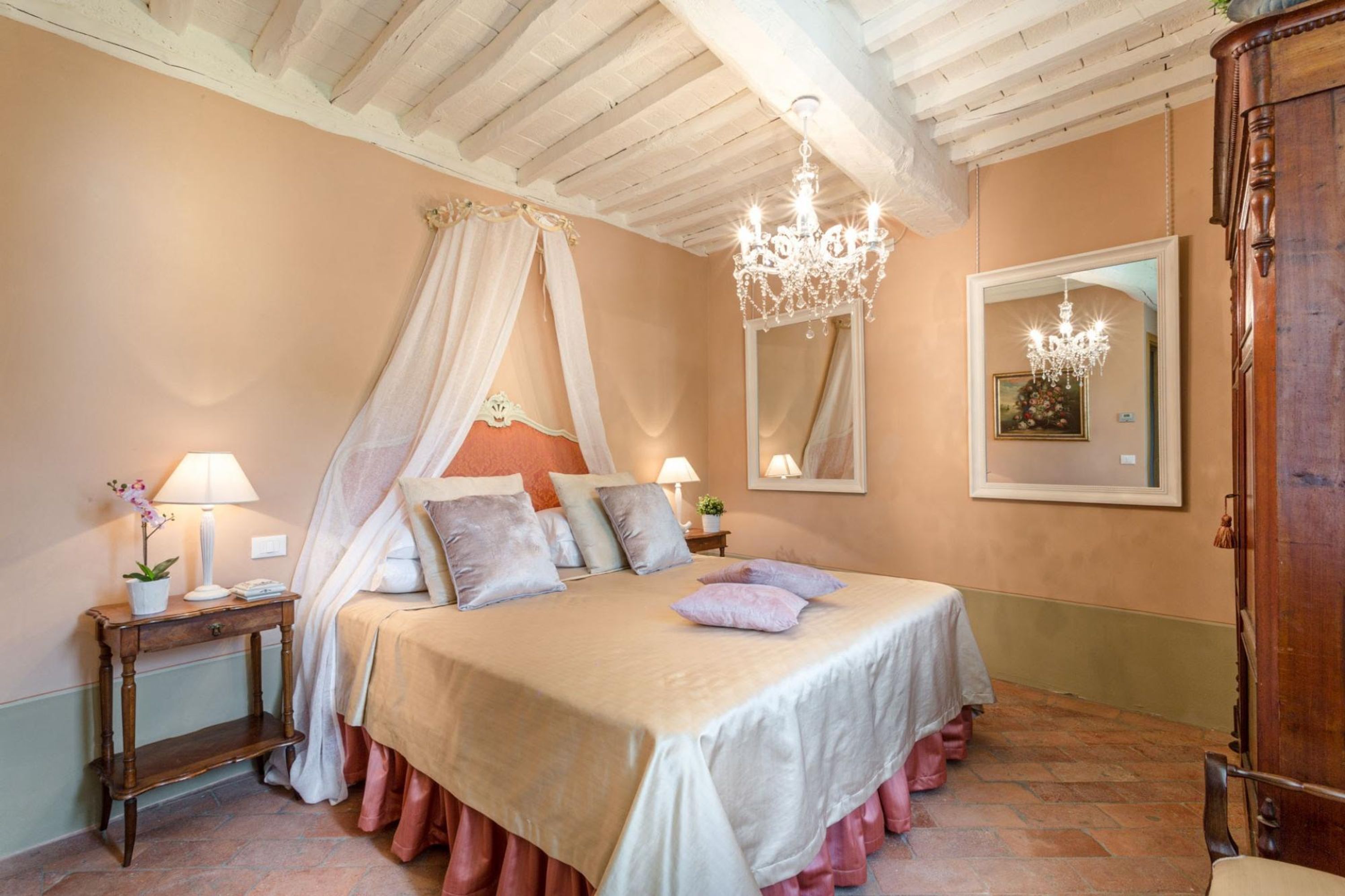A bedroom with a four-poster bed, a chandelier, a mirror, and a wooden wardrobe.