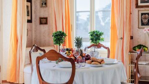 A dining table set with plates, glasses, and fruits, surrounded by orange curtains and framed pictures on the walls. - La Casa in Centro in Lucca (Lucca)