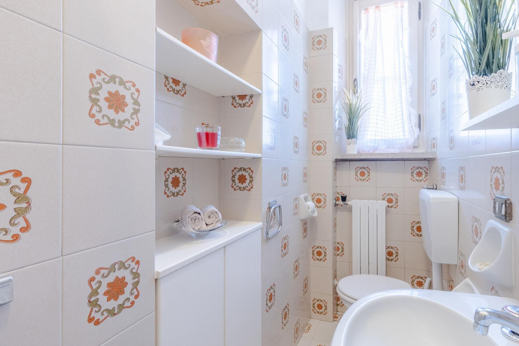 A bathroom with patterned tiles, a toilet, a sink, and a shelf with toiletries.