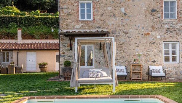 A stone building with a pool, a covered seating area, and a small garden.