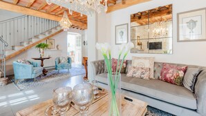 A spacious living room with a staircase, a chandelier, and a large mirror.