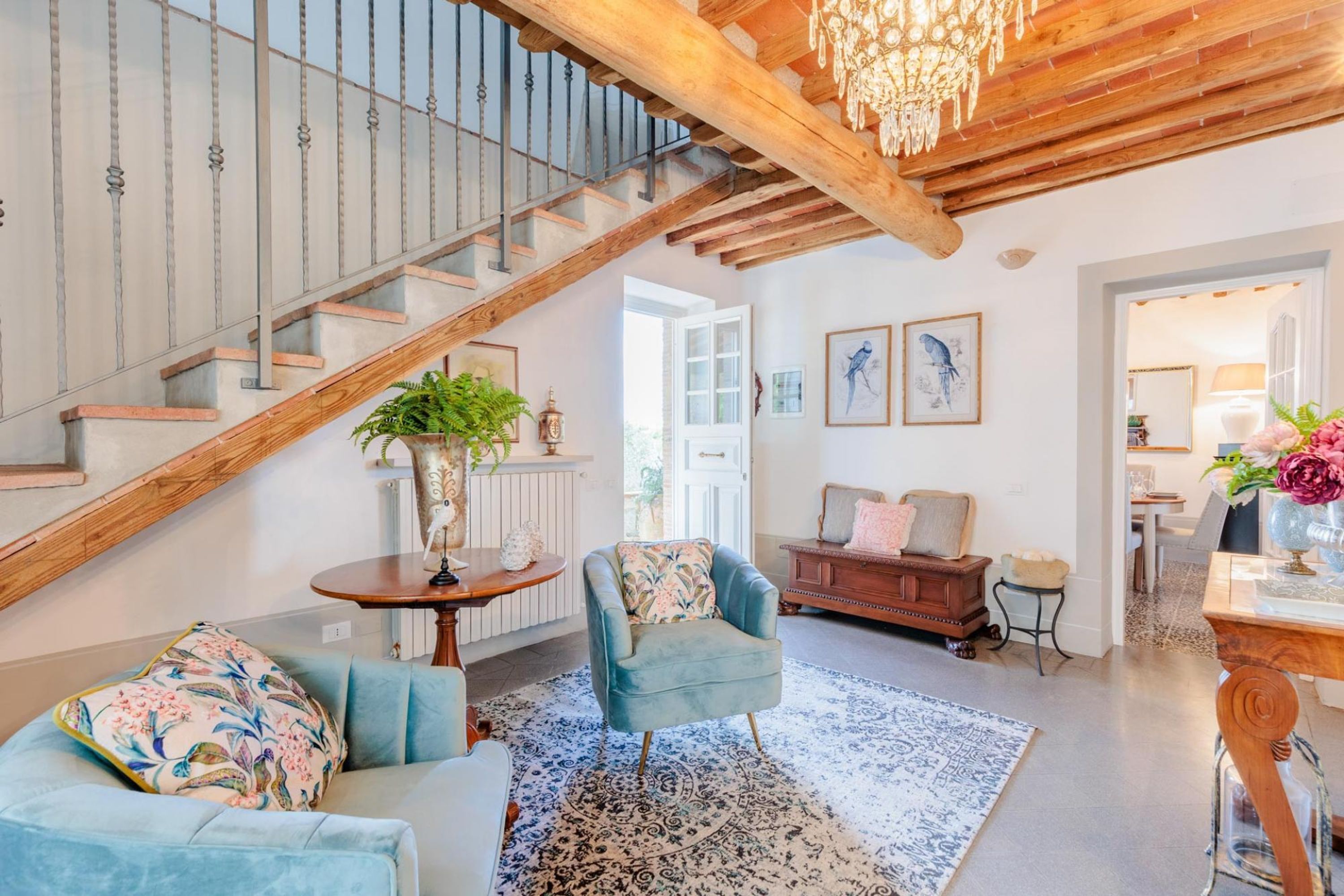 A spacious living room with a staircase, a chandelier, and a view of the outside.