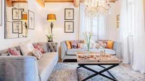 A cozy living room with a grey sofa, a wooden coffee table with decorative items, a chandelier, and framed pictures on the wall.