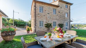 A stone building with a dining table set outdoors, surrounded by wicker chairs.