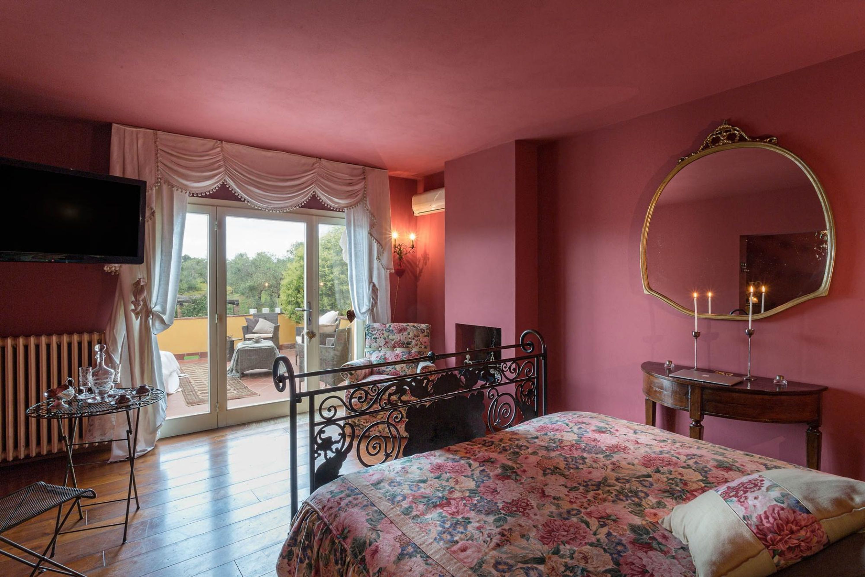 Une chambre à coucher avec un lit, une télévision, un miroir et une table sur laquelle est posé un vase.