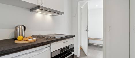 A modern kitchen with white cabinets, a stainless steel kettle, a cutting board with lemons, and a drying rack.