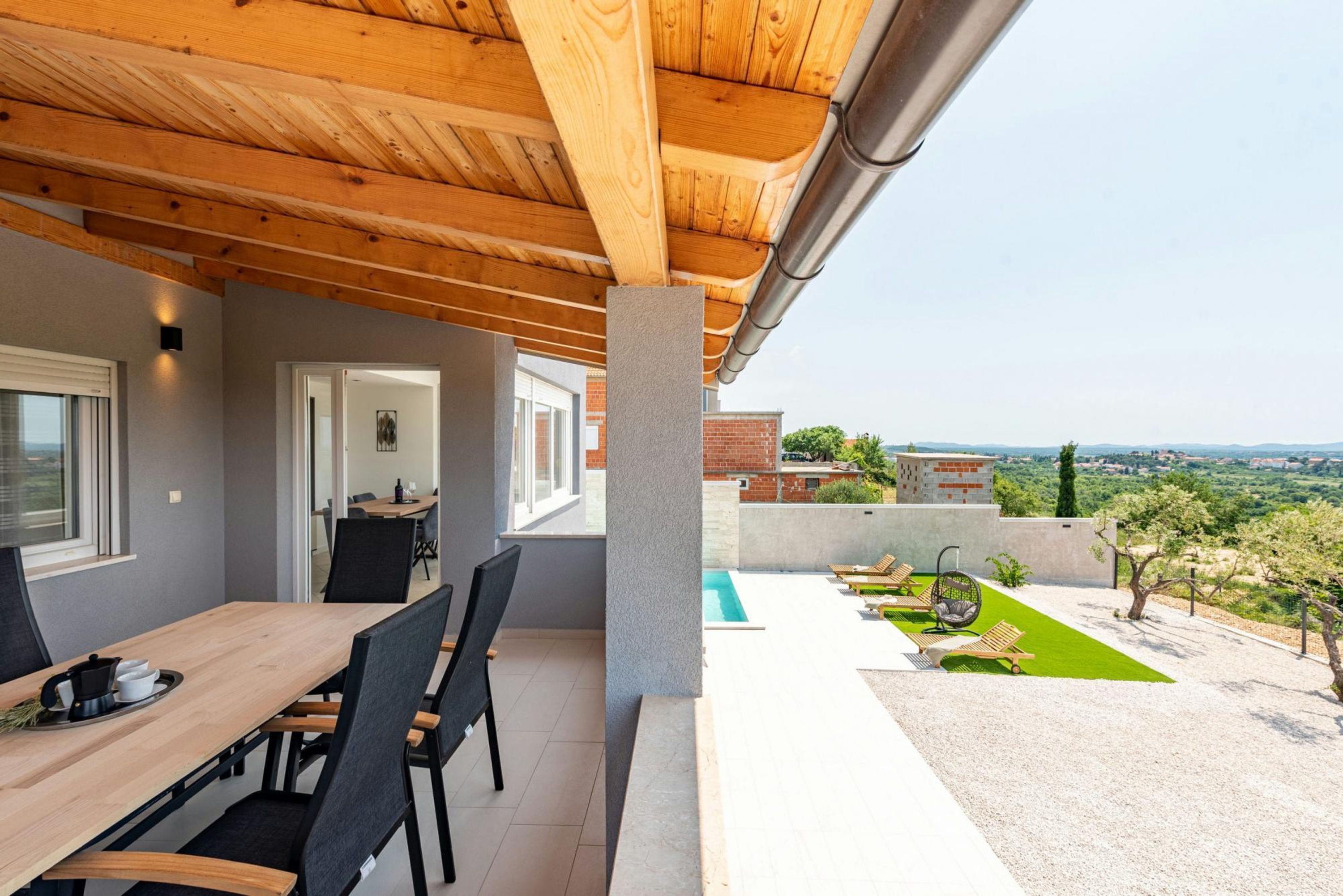 A covered outdoor dining area with a pool and garden view.