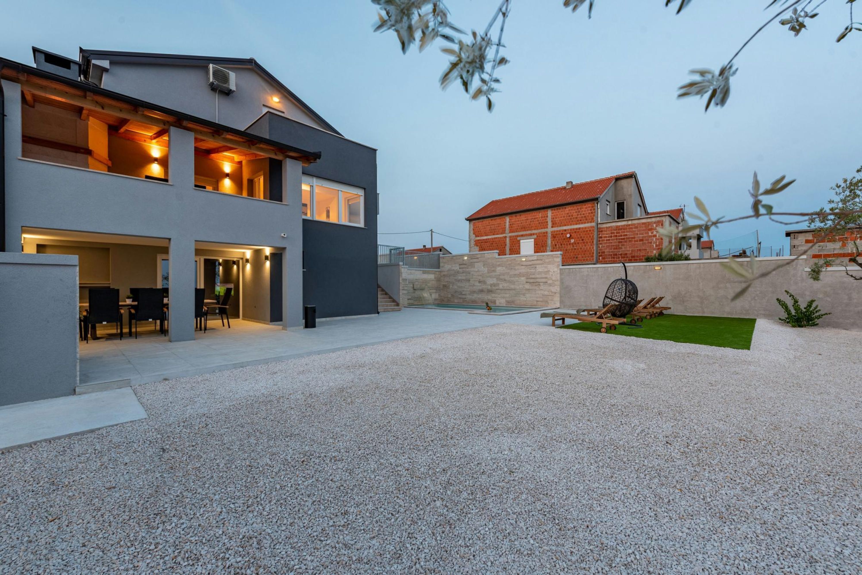 A modern two-story house with a gravel driveway, outdoor seating area, and a small garden.