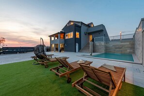 Una casa moderna de dos pisos con piscina, mobiliario exterior y un césped bien cuidado.