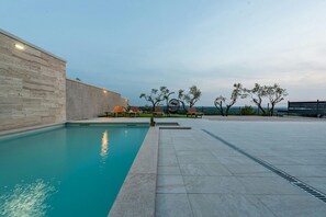 A swimming pool with a stone wall on one side, outdoor seating, and trees in the background. - Villa Pezer Zadarvillas (Benkovac)