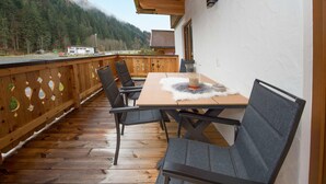 Eine Holzdiele mit Tisch und Stühlen, mit Blick auf eine bewaldete Berglandschaft.