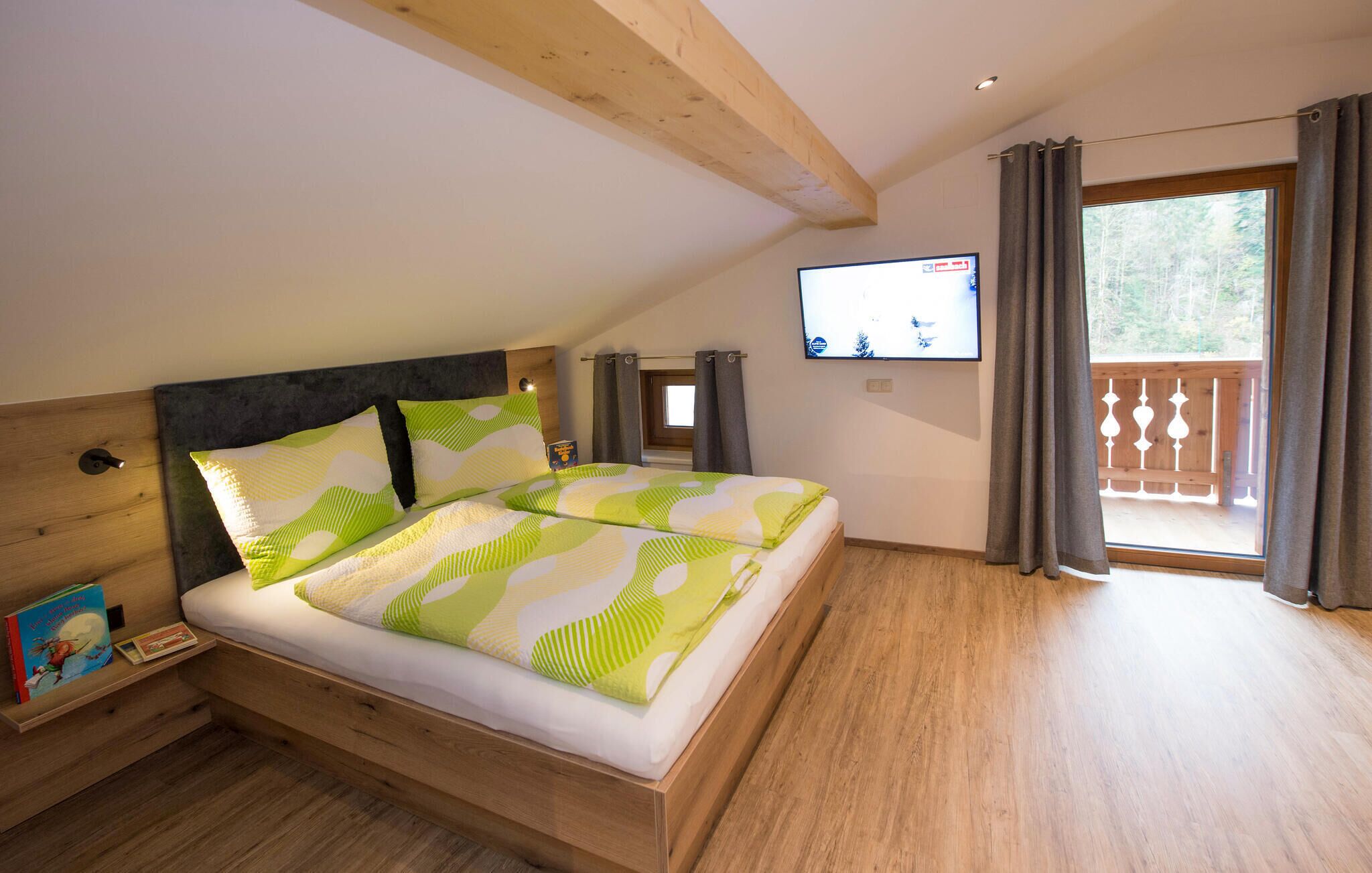 A bedroom with a wooden bed, a television on the wall, and a balcony with curtains.