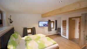 Ein Schlafzimmer mit einem Bett, einem Fernseher, einem Sessel und einer Holzbalkendecke.