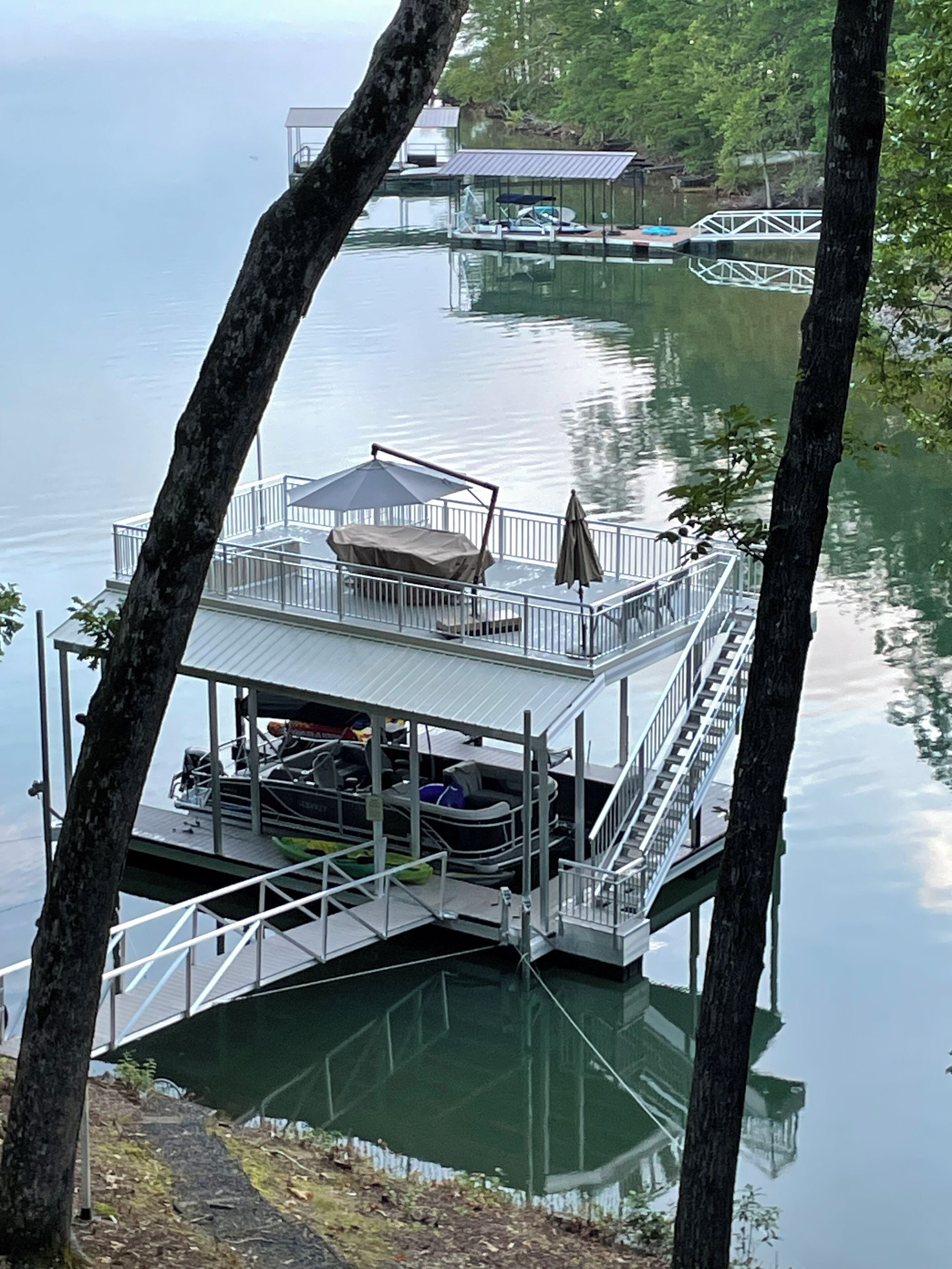 A dock with a covered seating area, a boat, and a small building in the background.