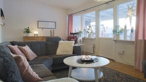 Un salon moderne avec un canapé gris, une table basse blanche et une grande fenêtre agrémentée de rideaux.