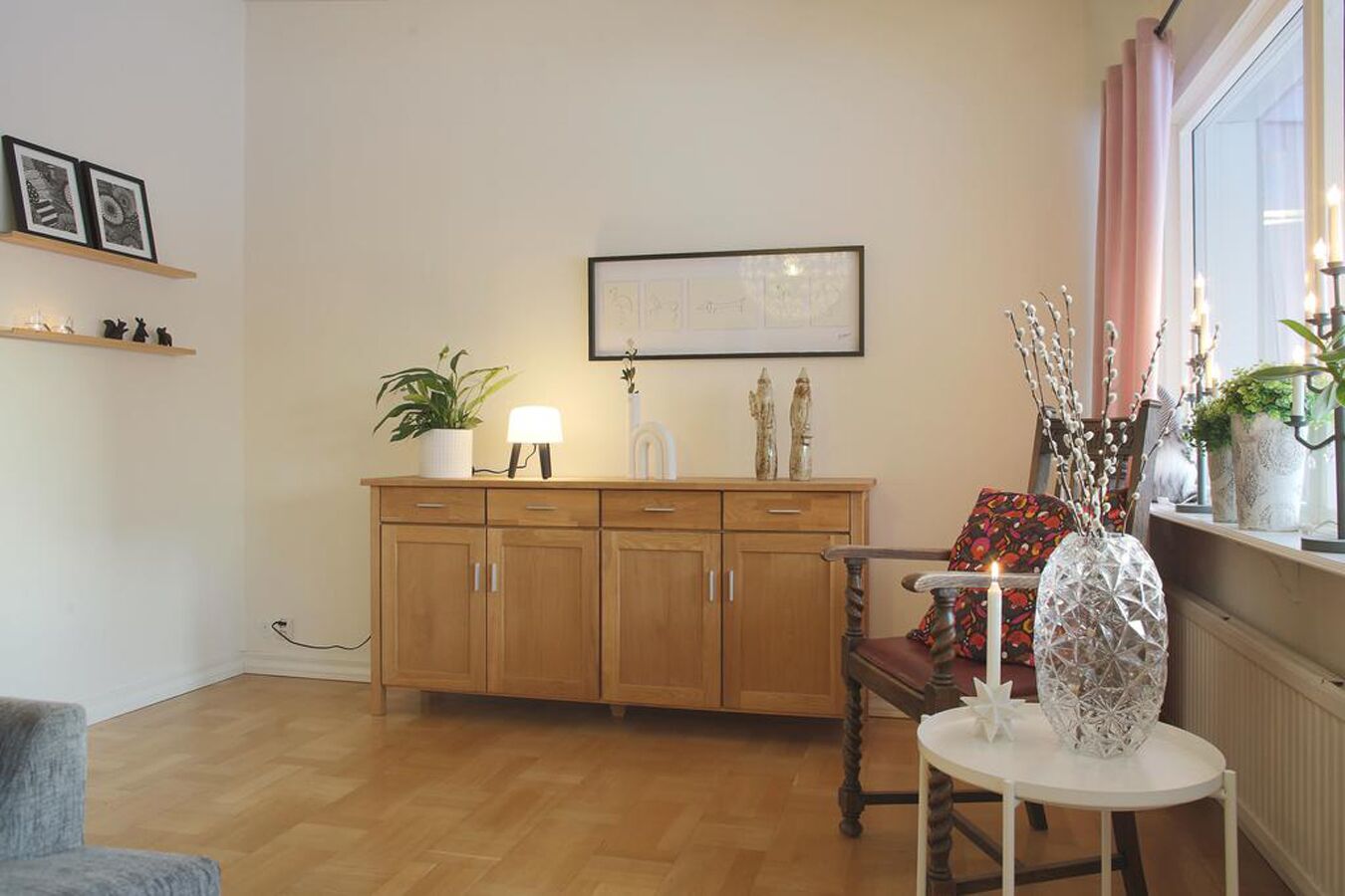Un salón acogedor con un aparador de madera, una silla, una mesa y un ventanal con cortinas.