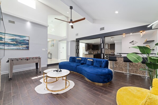 A modern living room with a blue sofa, a foosball table, and a yellow armchair.