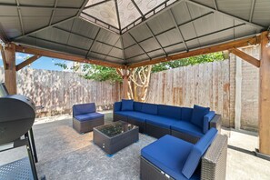 An outdoor patio with a covered seating area, a grill, and a wooden fence in the background.