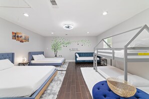 A modern hotel room with bunk beds, a blue sofa, a decorative wall mural, and a white rug.