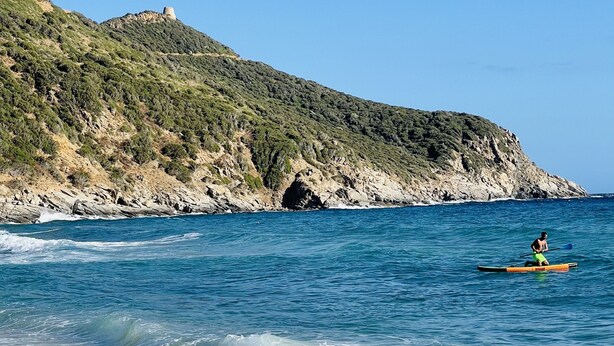 Une plage avec une falaise rocheuse et une personne pratiquant le kayak.