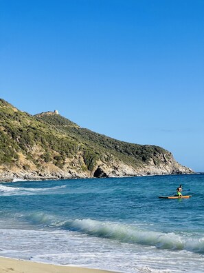 A beach with a rocky cliff and a person kayaking. - Detached villa with garden and sun deck - 6 guests - Solanas (Solanas)