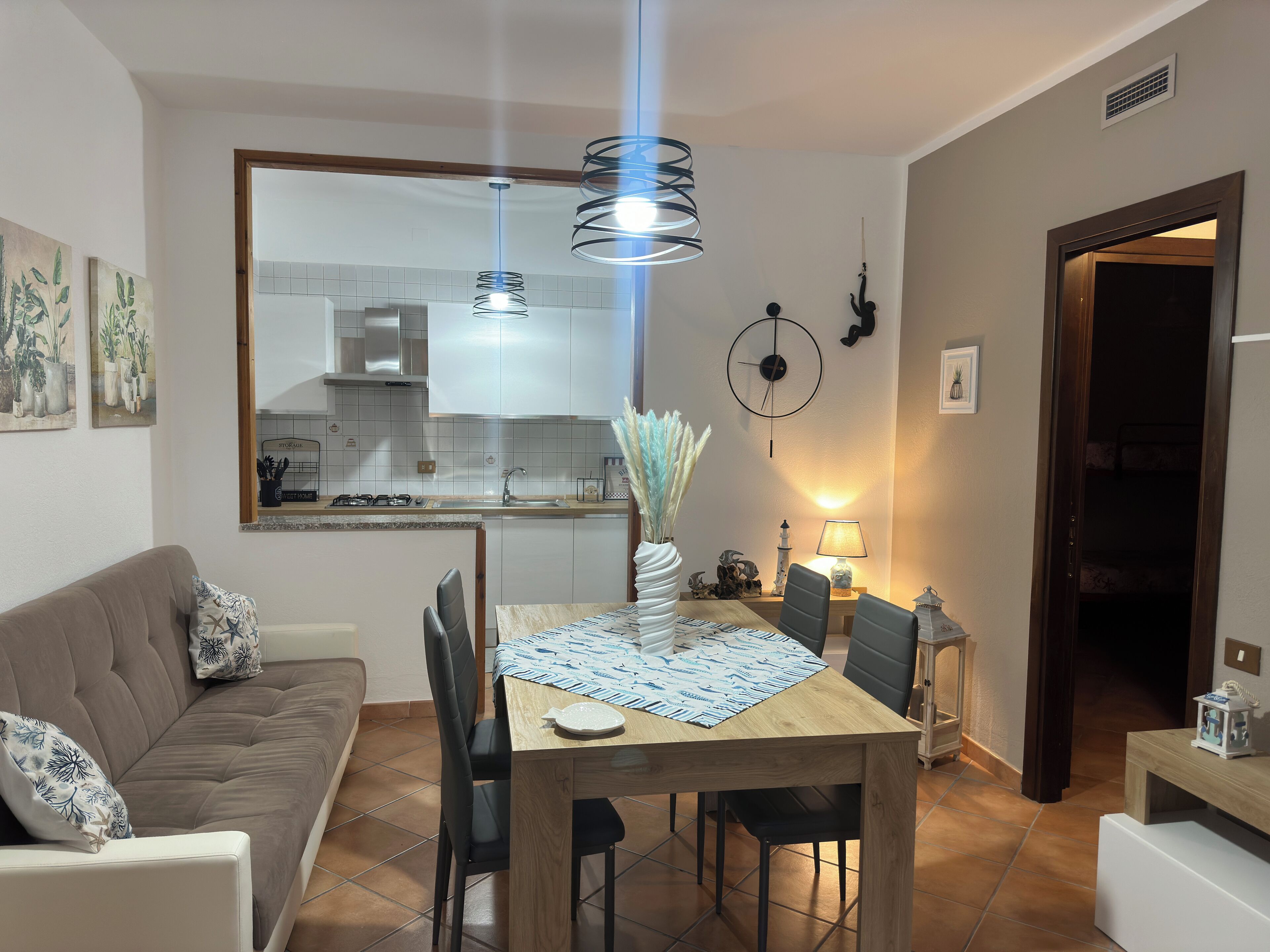 A modern living room with a sofa, dining table, chairs, and a kitchen in the background.