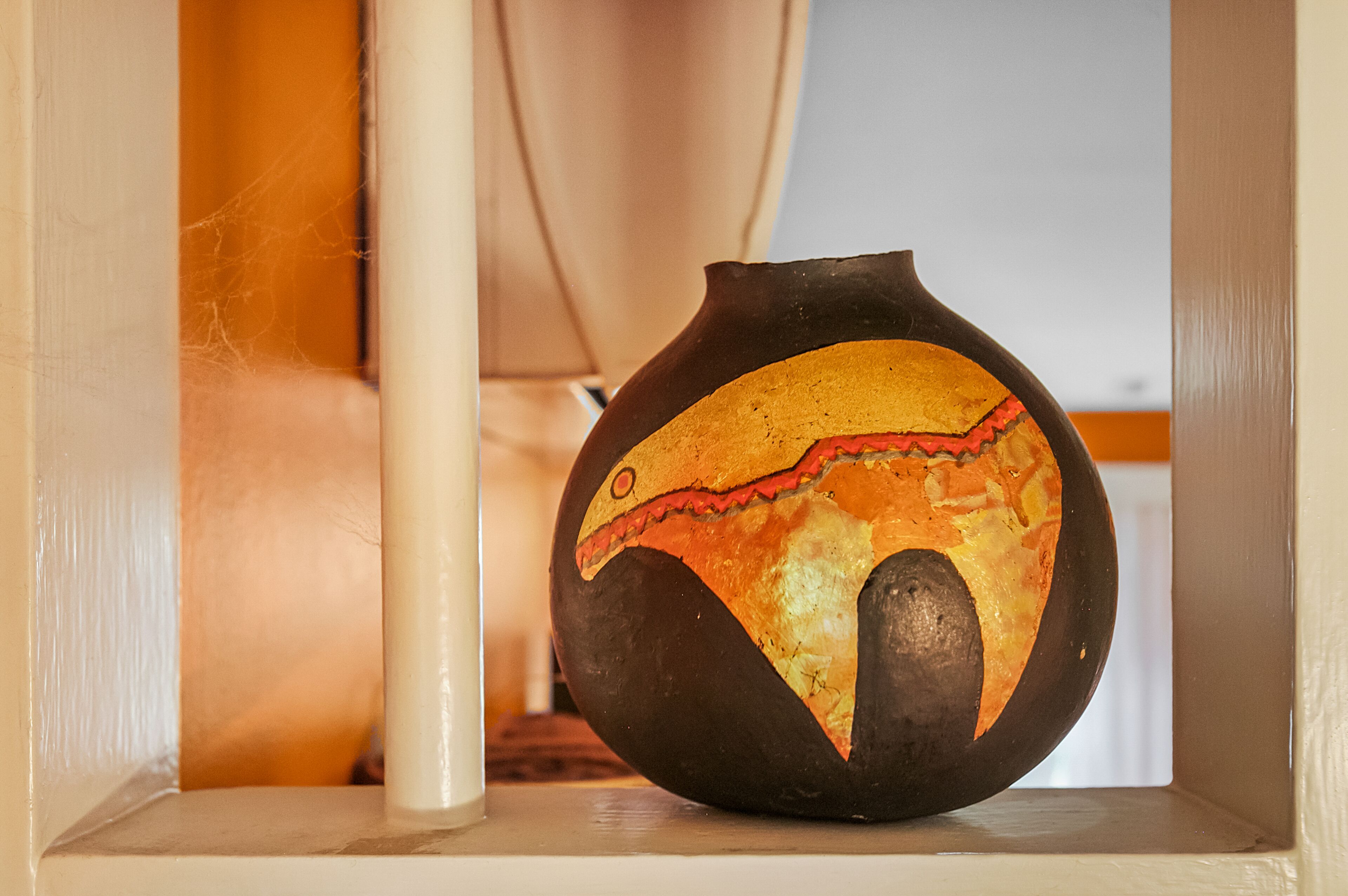A ceramic vase with a painted design, placed on a shelf.