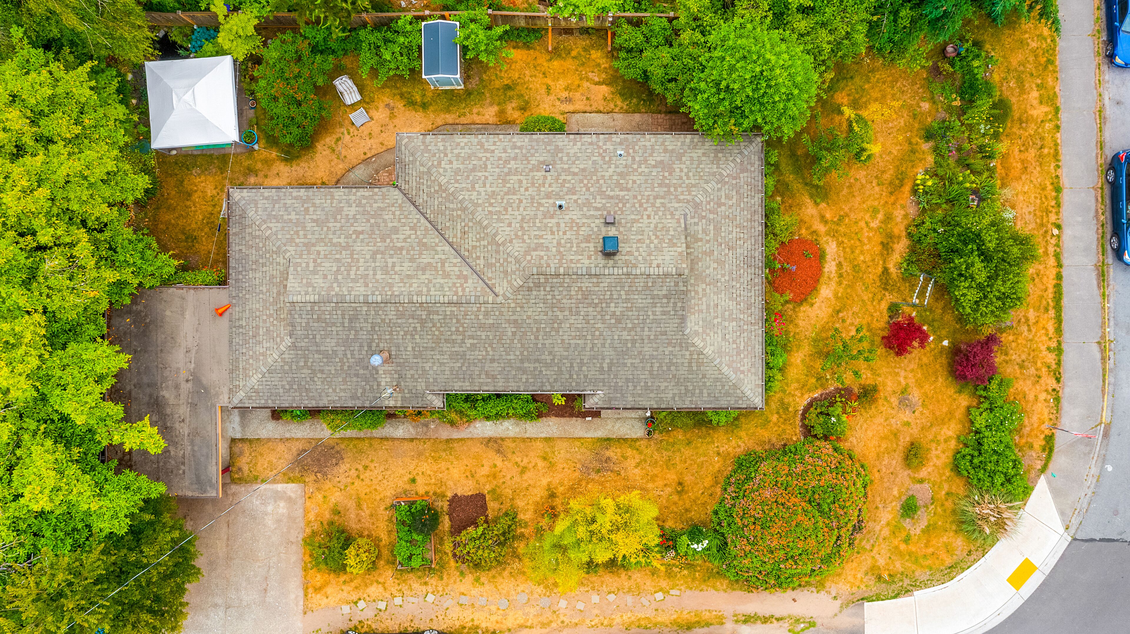 Luchtbeeld van een huis met schuin dak, omgeven door een tuin met verschillende planten en een verharde oprit.