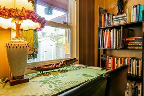 A room with a window, a bookshelf, a table with a green tablecloth, and a lamp.