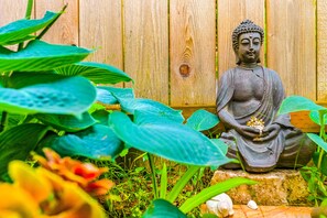 A Buddha statue in a garden setting with wooden fence and lush green foliage.
