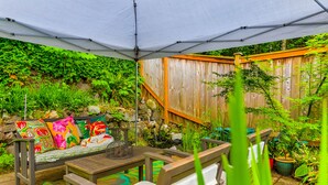 A covered patio area with a wooden bench, a table, and various potted plants. - Boho Bliss Bungalow (Shoreline)