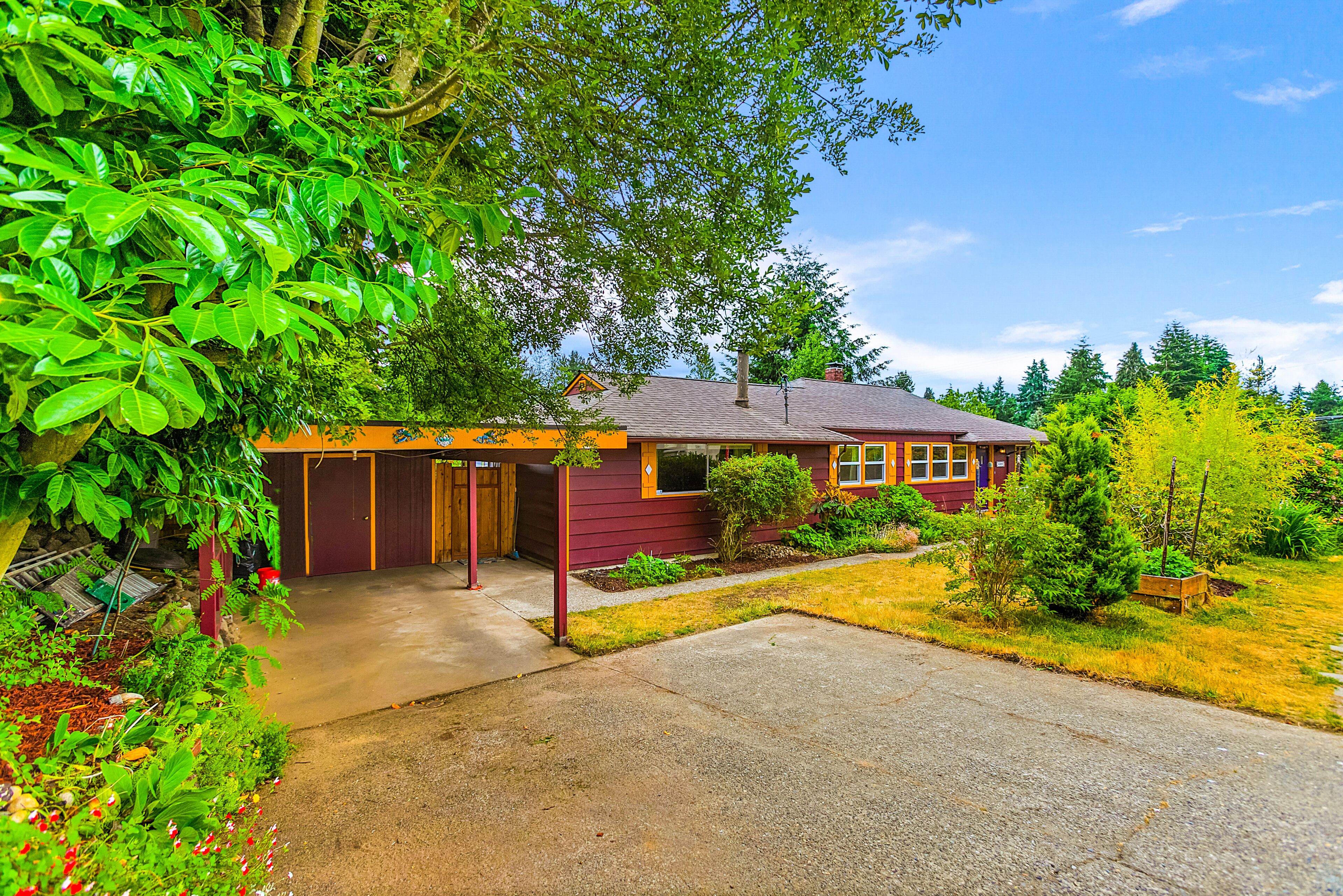 A single-story house with a garage, surrounded by lush greenery and a clear sky.
