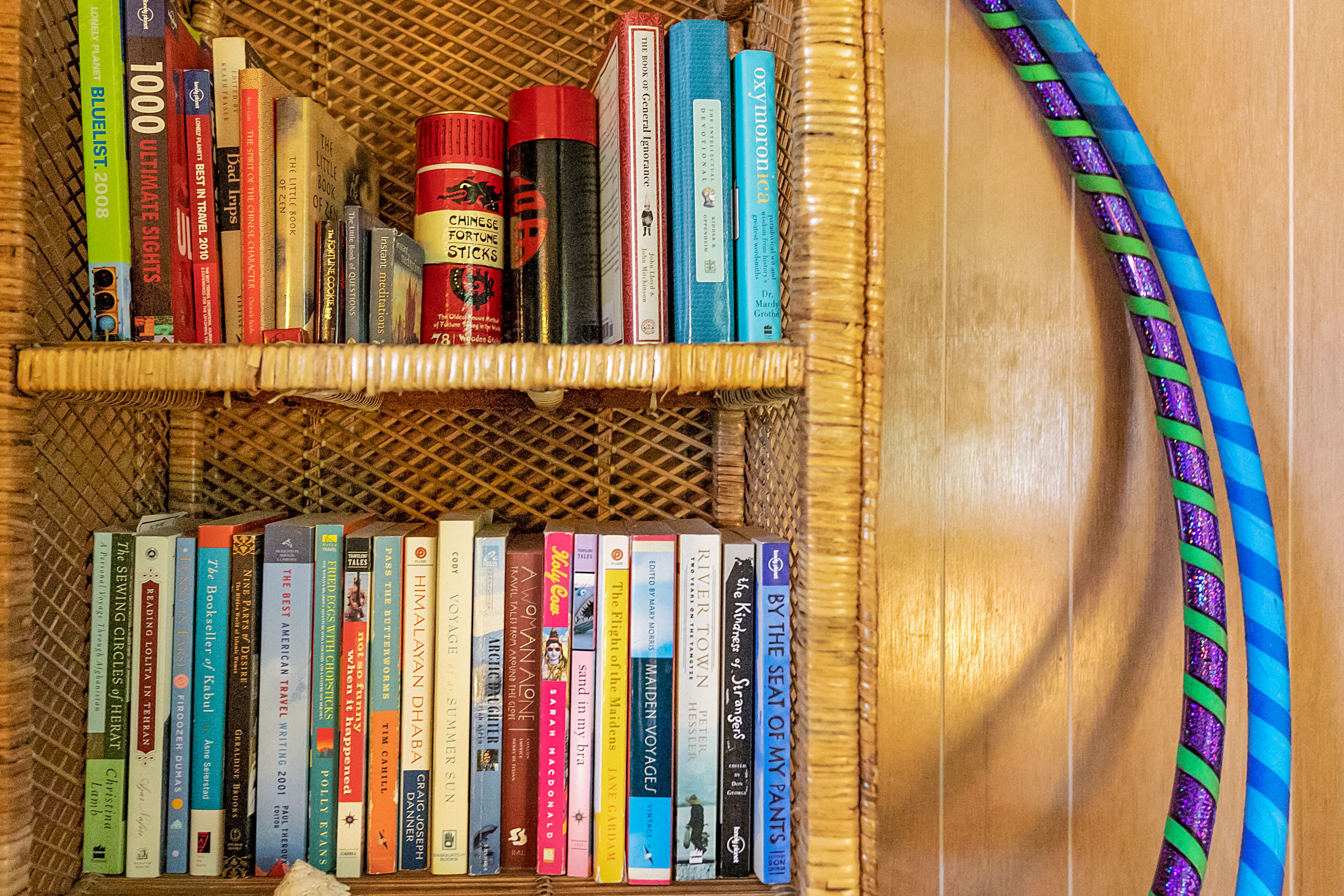 A wicker bookshelf filled with books and a small red container.