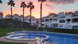 Una piscina de diseño circular, rodeada de palmeras y una zona residencial con edificios de varios pisos.
