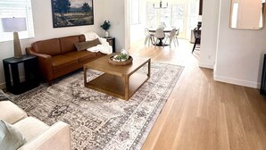 En stue med en brun sofa, et sofabord, et mønstret tæppe, en loftventilator og et spiseområde i baggrunden.
