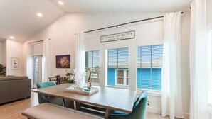 Et moderne spiseområde med et træbord, teal stole og en bænk. Store vinduer med blå skodder og udsigt udad.