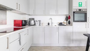 A modern kitchen with white cabinets, a red microwave, a coffee maker, a kettle, and a toaster. - Stylish Top-Floor Flat (South Harrow)
