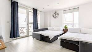A modern bedroom with two beds, a sliding glass door, a clock, and a small balcony. - Stylish Top-Floor Flat (South Harrow)