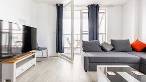 A modern living room with a flat-screen TV, grey sofa, and a balcony with curtains. - Stylish Top-Floor Flat (South Harrow)