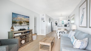 En moderne stue med et træbord, en grå sofa og et stort maleri af en strand.