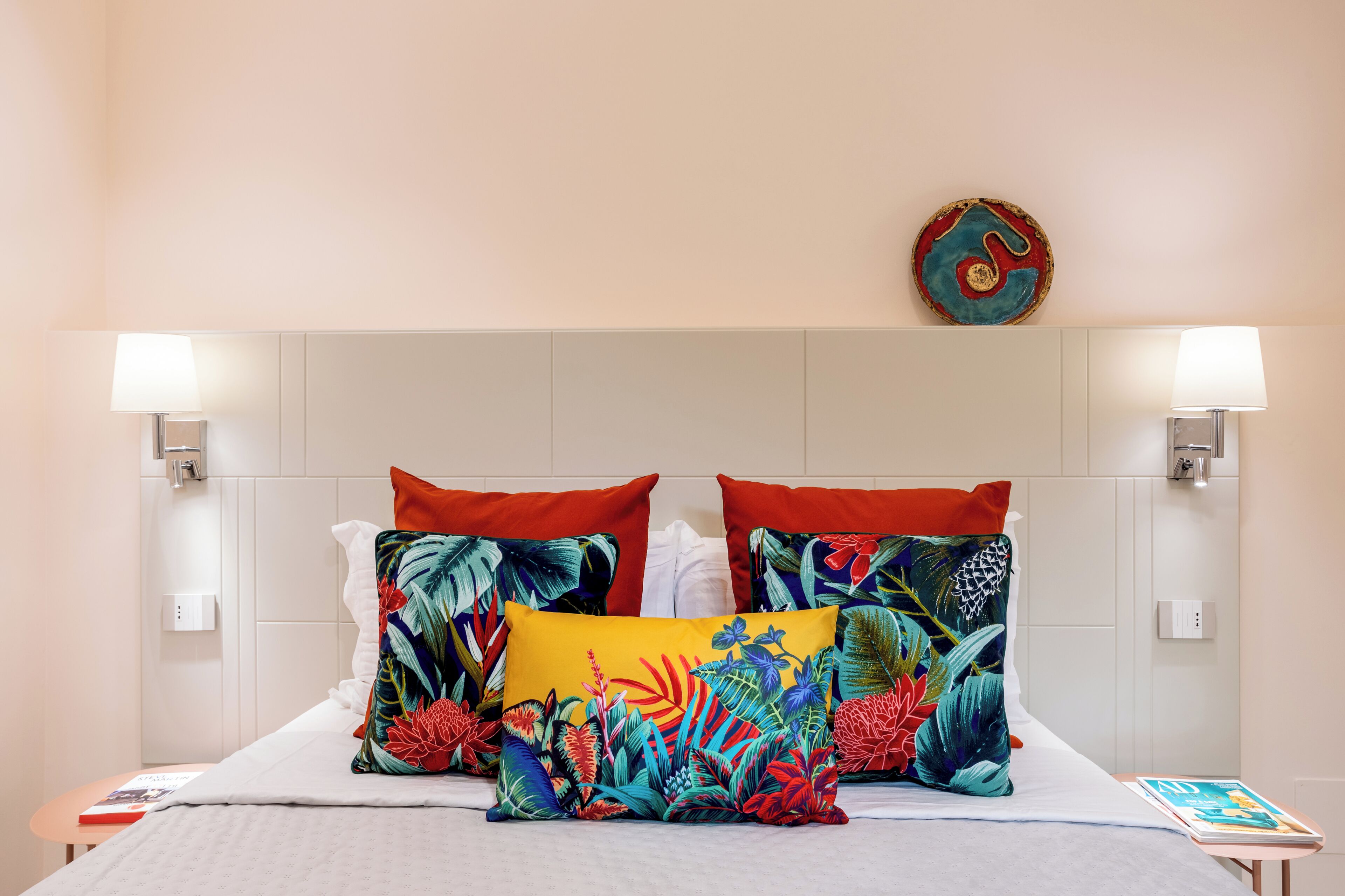 A bed with multiple pillows, two wall-mounted lamps, and a wall art piece.