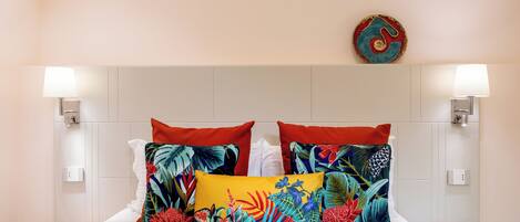 A bed with multiple pillows, two wall-mounted lamps, and a wall art piece.
