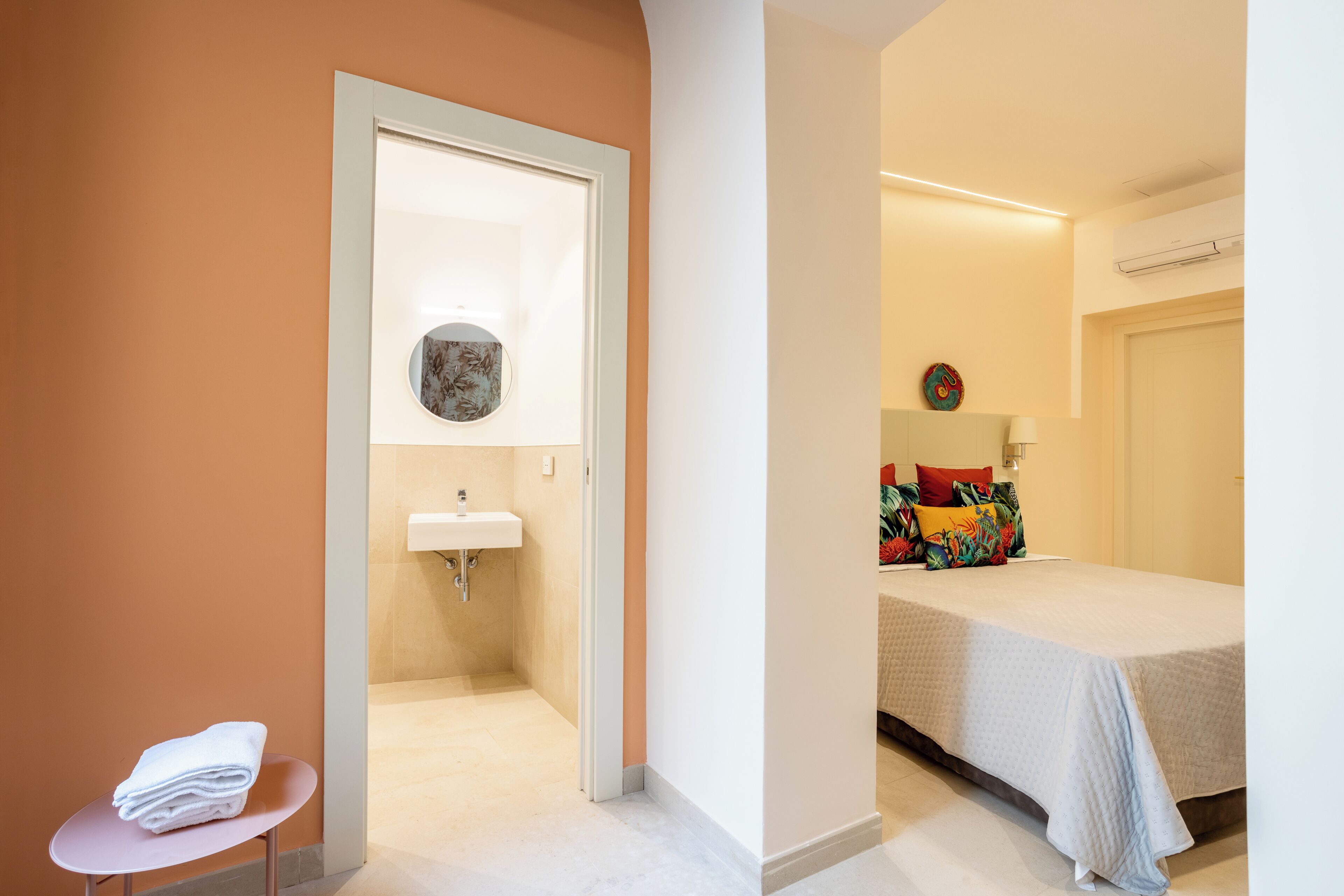 Ein Hotelzimmer mit Bett, einem kleinen Tisch mit Handtüchern, einem Badezimmer mit Waschbecken und einem Spiegel.