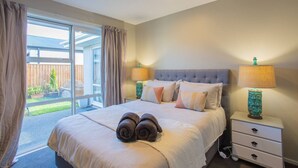 Une chambre à coucher avec un grand lit, deux tables de chevet, une fenêtre avec des rideaux et une vue sur l’extérieur.