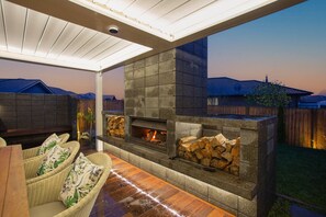 Un patio al aire libre con chimenea de piedra, mobiliario de mimbre y vistas a casas vecinas.
