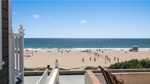 Une vue sur la plage depuis un balcon, avec une tour de surveillance des sauveteurs, une plage de sable et des gens.