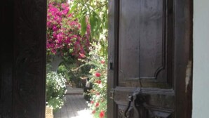 Una puerta de madera con intrincados grabados, que da a un jardín con flores rosadas y un camino.