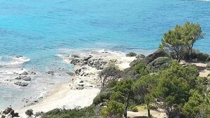 Un paisaje costero con aguas azul cristalino, costa rocosa y vegetación escasa, incluyendo pinos.