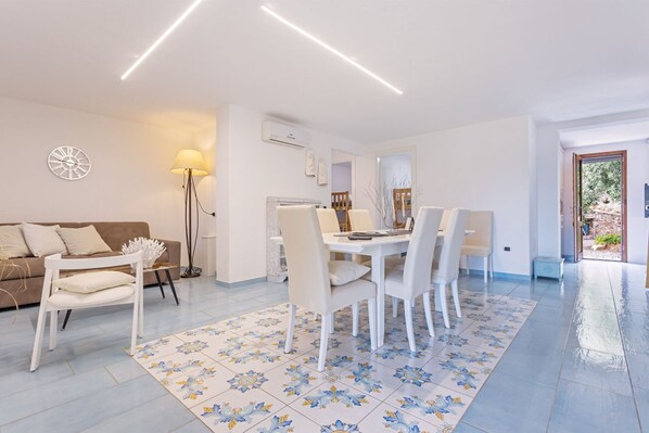 A modern living room with a dining area, a sofa, a lamp, and a patterned rug.